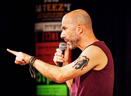 תמונת מופע: תמונה של דרור קרן מחזיק מיקרופון ביד ומצביע