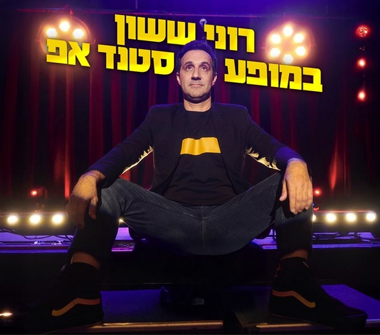 תמונת מופע: רוני ששון יושב על הבמה ברגליים פשוקות לצדדים