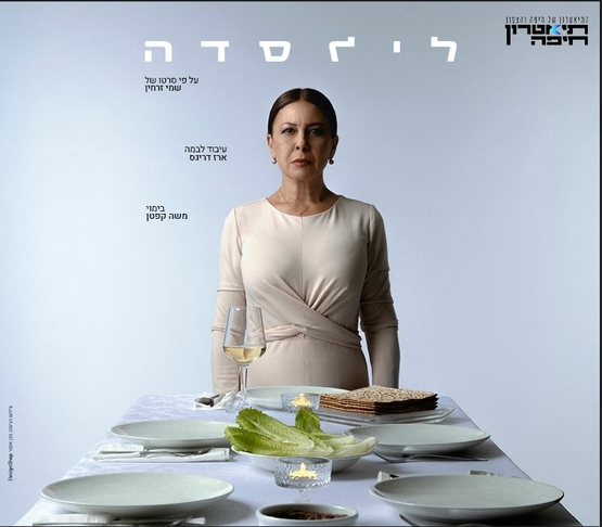 תמונת מופע: בחורה עומדת מסתכלת קדימה ולפניה שולחן ערוך עם צלחות וכוס יין