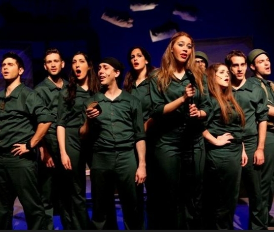 תמונת מופע: שחקני ההצגה בלבוש מדים שרים על הבמה